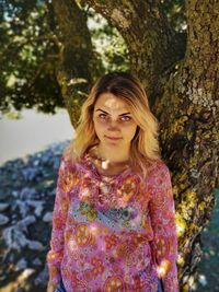 Young woman standing against tree trunk