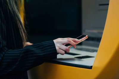 Hands of an anonymous person using a mobile phone at an atm