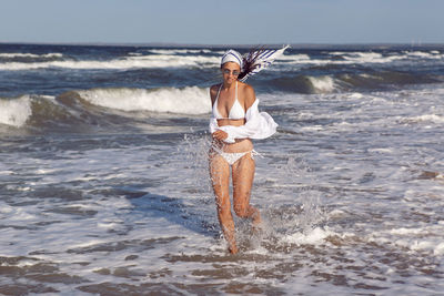 Woman run in a white bathing suit and hat sunglasses on an empty sandy beach