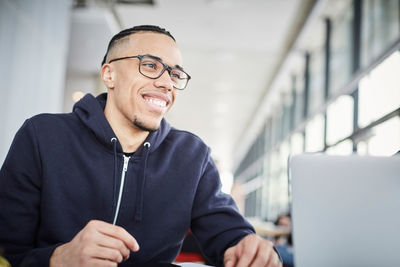 Smiling young university student looking away while sitting at table in cafeteria