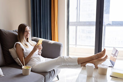 Full length of woman using mobile phone while sitting on sofa