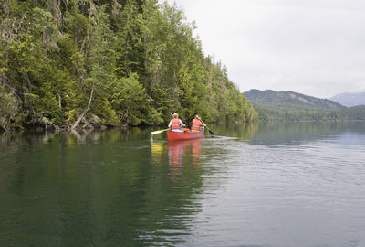 People on boat sailing in lake against sky