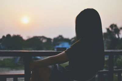 Side view of silhouette woman sitting by railing in balcony at sunset