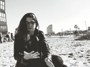 Young woman looking at palm while sitting at beach against w barcelona