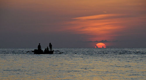 Silhouette people in sea against sky during sunset