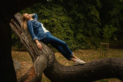 Side view of young woman sitting on tree trunk