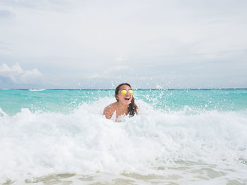Young woman swimming in sea against cloudy sky