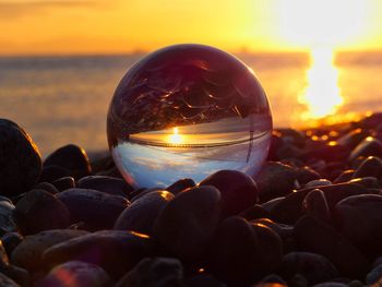 Close-up of crystal ball on beach against sky during sunset