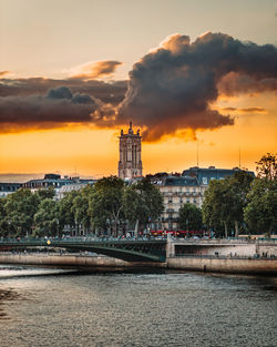 Buildings by river against sky during sunset