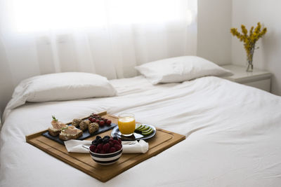 Breakfast tray with fruit and toasts on a bed in a white room