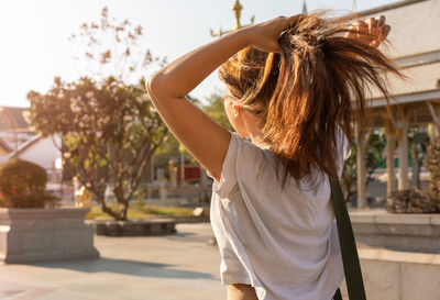 Rear view of woman tying hair while standing in park