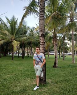 Full length portrait of young man standing on palm trees