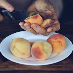 Cropped image of hand cutting peach on table