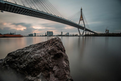 Low angle view of bridge over river in city against cloudy sky