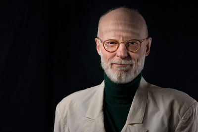 Portrait of smiling senior man wearing suit against black background