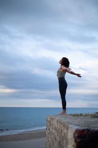 Rear view of woman standing on rock by sea against sky