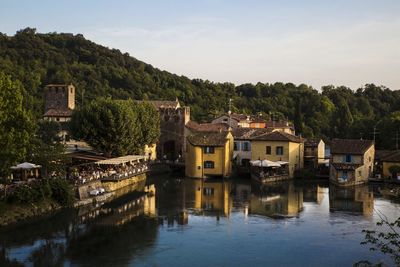 Houses by lake and buildings against sky