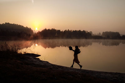 Man standing on lake against sky during sunset