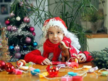Little girl in santa claus hat rejoices and plays with christmas balls and a toy dog. 