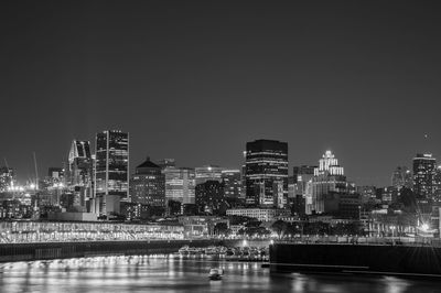 River by illuminated buildings against clear sky at night