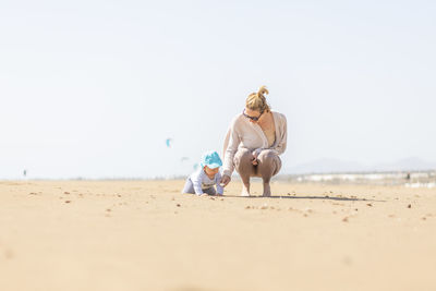 Rear view of woman sitting at beach against clear sky