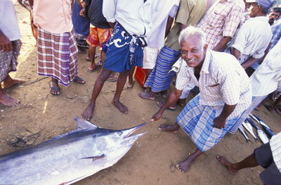 Portrait of happy fisherman with dead swordfish at beach surrounded with crowd