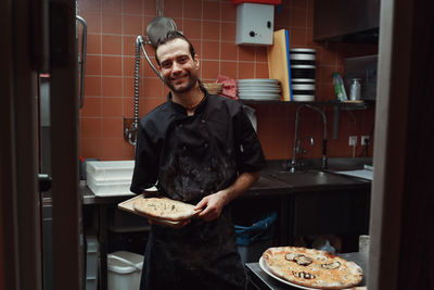 Handsome pizzaiolo making pizza at kitchen in pizzeria.