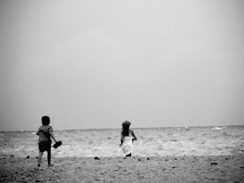 Rear view of children running at beach against clear sky