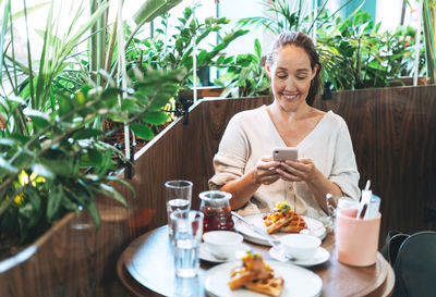 Young woman using mobile phone while sitting on table