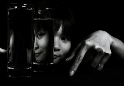 Close-up of young woman gesturing by drinking glasses against black background