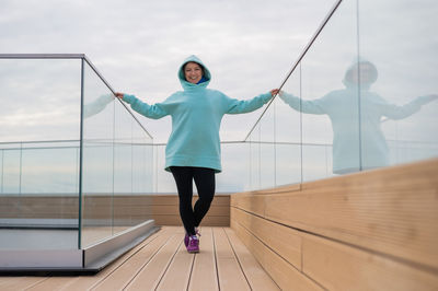 Portrait of woman standing by glass railing against sky