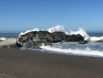 Scenic view of waves crashing on rocks  against clear sky