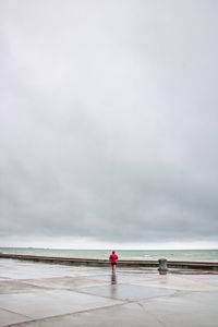 Rear view of woman walking on promenade against cloudy sky