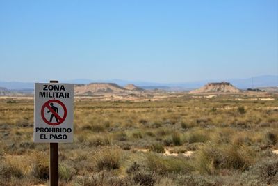 Warning sign on field against clear sky