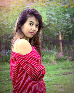 Portrait of young woman with long hair standing against plants in park