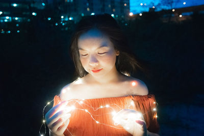 Young woman looking at illuminated camera at night