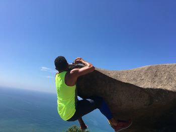 Low angle view of man on rock against clear blue sky