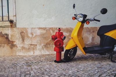 Motor scooter by fire hydrant on footpath by wall