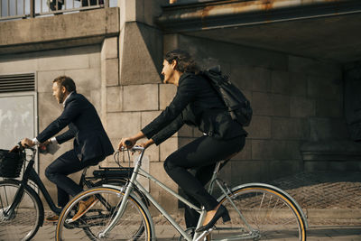 Side view of businessman and businesswoman riding bicycles on street in city