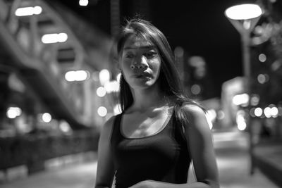 Portrait of young woman standing against illuminated city at night