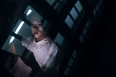 Young man with smart phone seen through glass at night