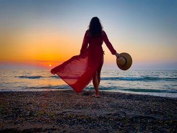 Woman with umbrella on beach against sky during sunset