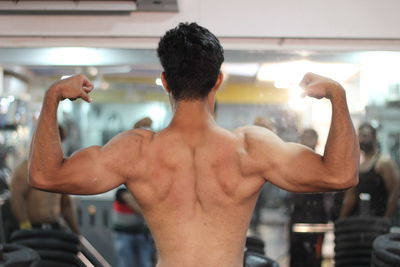 Rear view of shirtless young man flexing muscles at gym