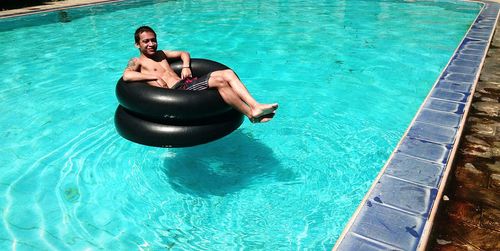 High angle portrait of smiling young man sitting on inflatable ring in swimming pool