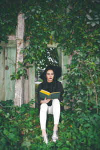 Young woman sitting on book against tree