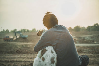 Rear view of woman sitting with dog at construction site against clear sky during sunset