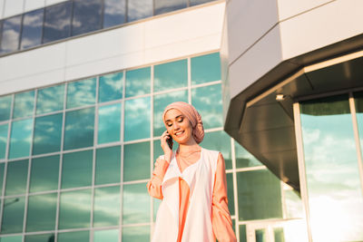 Young woman talking on phone while standing against building