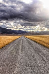 Country road amidst landscape against sky