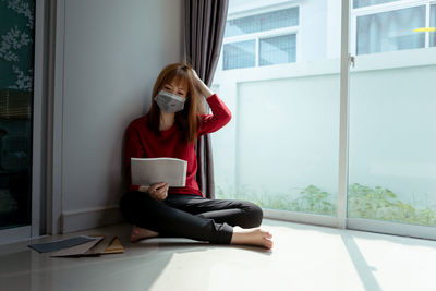 Young woman using mobile phone while sitting on window