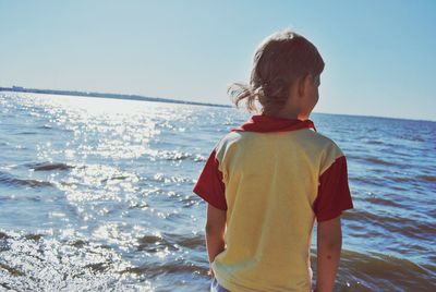 Rear view of boy standing by sea against sky